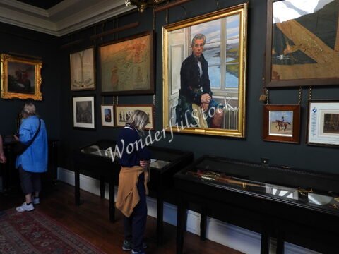 Un homme en kilt est représenté sur un tableau dans le château de Dunvegan, Écosse, avec des visiteurs observant des œuvres d'art.