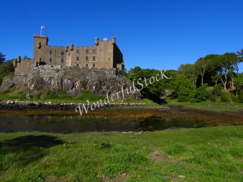 Château de Dunvegan en Écosse, construit sur un promontoire rocheux, entouré de verdure et d'un cours d'eau.