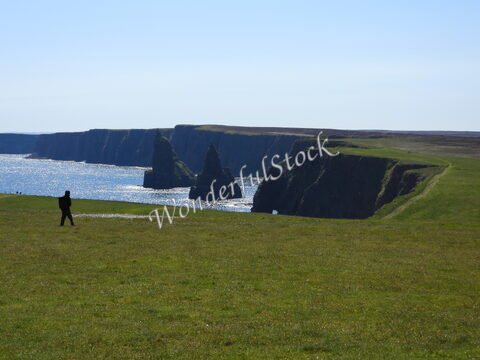 Falaises de Duncansby en Écosse, avec un promeneur sur une pelouse verdoyante et la mer en arrière-plan.