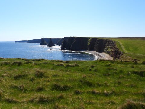 Falaises de Duncansby Head en Écosse, avec une mer calme et des rochers émergeant de l'eau.