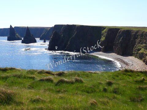 Falaises et formations rocheuses à Duncansby Head, Écosse, avec une plage de galets et de l'herbe verte au premier plan.