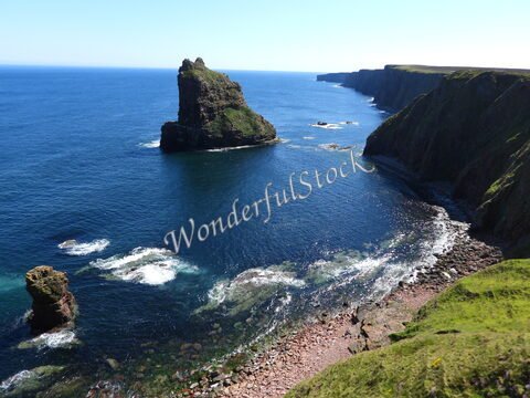 Un promontoire rocheux surplombe la mer à Duncansby Head, Écosse, avec des falaises verdoyantes et des eaux bleues.