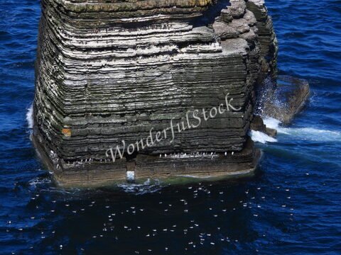 Rochers stratifiés au Duncansby Head en Écosse, entourés par des eaux marines et quelques oiseaux en vol.
