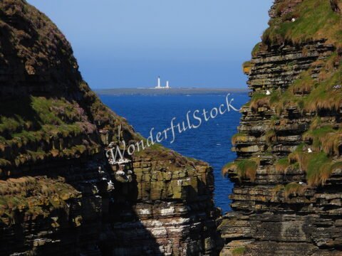 Falaises de Duncansby Head en Écosse, avec un phare visible au loin et la mer en arrière-plan.