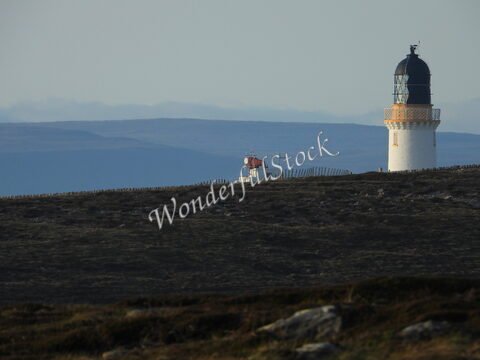 Phare à Dunnet Head, Écosse, sur une colline avec des montagnes en arrière-plan.