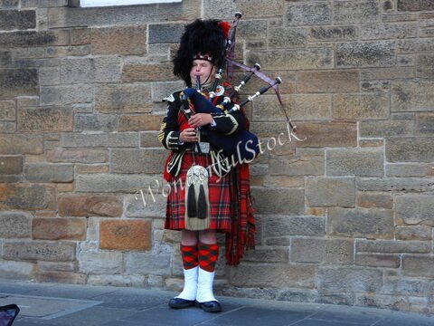 Musicien en kilt jouant de la cornemuse sur un mur de pierre à Édimbourg, Écosse.