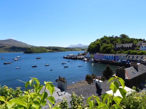 Bateaux dans le port coloré de l'île de Skye, Écosse, avec des collines verdoyantes en arrière-plan.