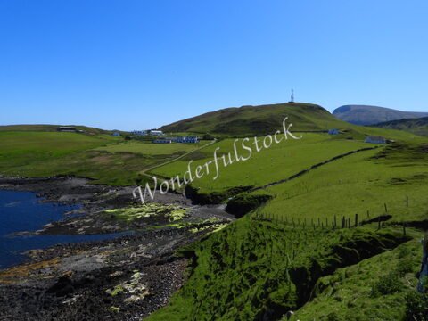 Pâturages verdoyants et côtes rocheuses sur l'île de Skye, Écosse. Un paysage rural avec quelques maisons blanches en arrière-plan.