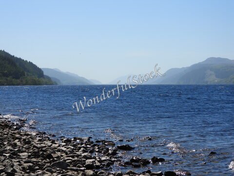 Loch Ness en Écosse, avec des collines verdoyantes en arrière-plan et des rochers au bord de l'eau.