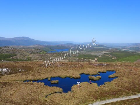 Lac et paysages vallonnés en Écosse, avec des personnes près d'un plan d'eau et des montagnes en arrière-plan.