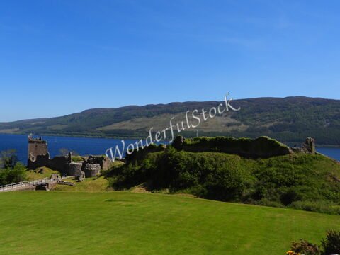 Ruines d'un château sur les rives du Loch Ness, Écosse, avec des collines verdoyantes en arrière-plan.