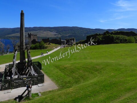 Un château en ruines surplombant le Loch Ness en Écosse, avec un terrain verdoyant et des visiteurs sur un chemin.