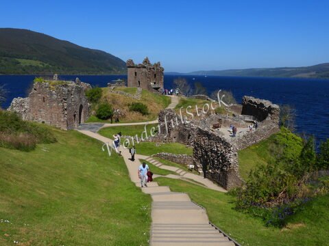 Ruines d'un château surplombant le Loch Ness en Écosse, avec des visiteurs se promenant sur un chemin en pente.