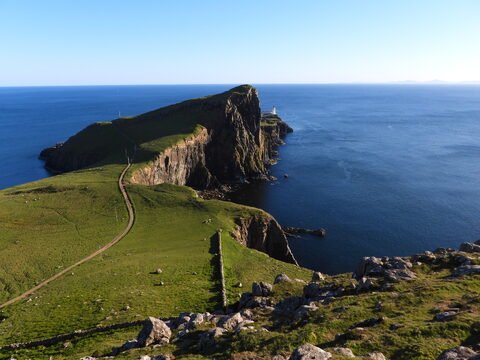 Falaises verdoyantes surplombant la mer à Neist Point, Écosse, avec un phare visible au loin.