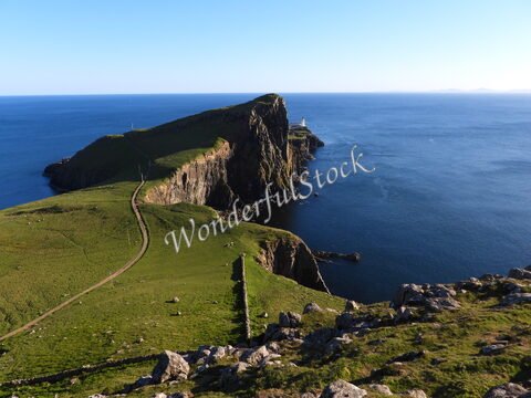 Falaises verdoyantes surplombant la mer à Neist Point, Écosse, avec un phare visible au loin.