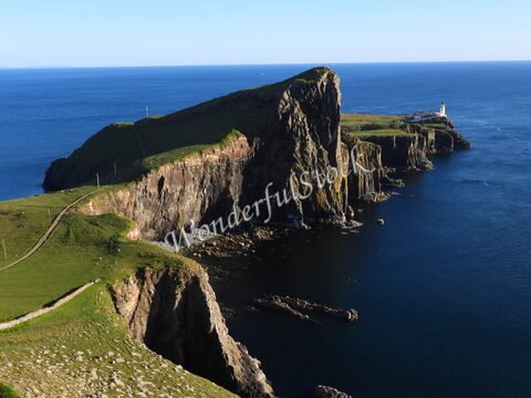 Falaises abruptes et phare à Neist Point, Écosse, surplombant une mer calme sous un ciel dégagé.
