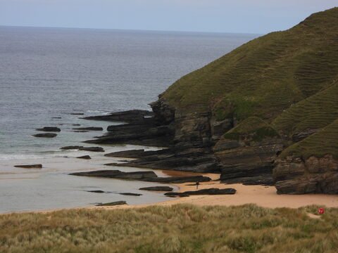 Plage de Strathy en Écosse, avec des rochers et des collines verdoyantes en arrière-plan.