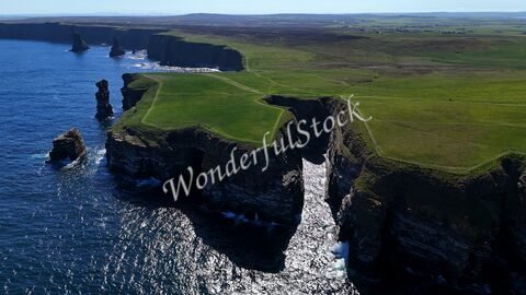 Falaises verdoyantes à Duncansby Head, Écosse, surplombant l'océan, avec des formations rocheuses distinctives et des vagues.
