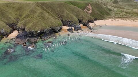 Plage de Strathy en Écosse, avec des rochers et des collines verdoyantes bordant l'eau turquoise.