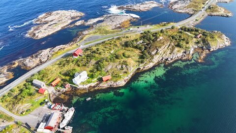 Vue aérienne de la route de l'Atlantique en Norvège, avec des maisons rouges et une mer turquoise entourée de rochers.