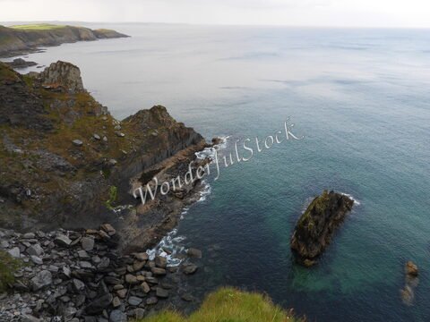 Falaises escarpées surplombant la mer à Irlande. Des rochers émergent des eaux calmes, avec des paysages verdoyants en arrière-plan.