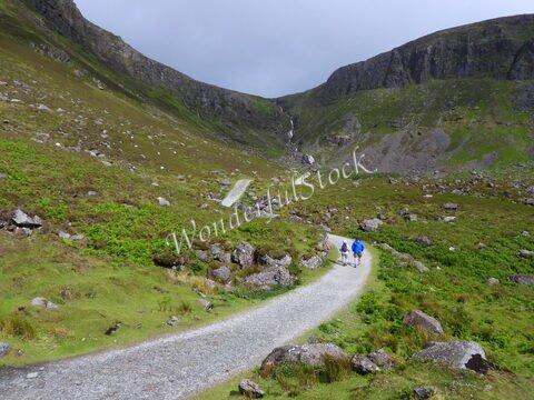Deux randonneurs marchent sur un chemin en gravier entouré de collines verdoyantes en Irlande.