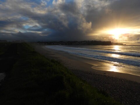 Plage de Ballycastle en Irlande, avec des vagues et un ciel nuageux illuminé par le soleil couchant.