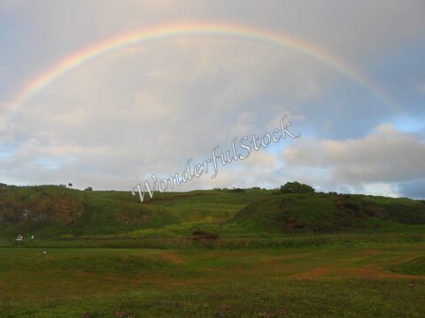 Un arc-en-ciel surplombe des collines verdoyantes à Ballycastle, en Irlande, avec un ciel nuageux en arrière-plan.