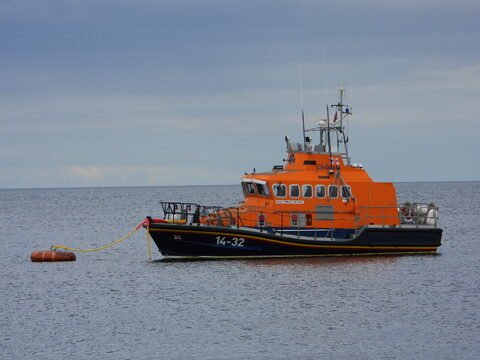 Bateau de sauvetage orange à Ballycastle, Irlande, flottant sur une mer calme avec un bouée à proximité.