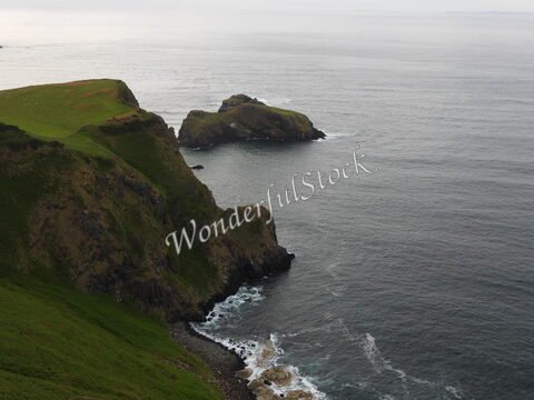 Falaises verdoyantes surplombant la mer à Ballycastle, Irlande, avec des rochers émergents dans l'eau.