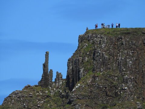 Colonne de pierres surplombant la Chaussée des Géants, en Irlande, avec des visiteurs au sommet de la falaise.