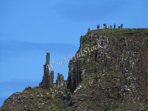 Colonne de pierres surplombant la Chaussée des Géants, en Irlande, avec des visiteurs au sommet de la falaise.