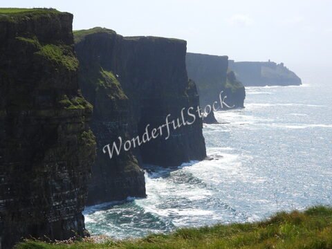 Falaises surplombant l'océan à Cliffs of Moher, Irlande, avec des formations rocheuses distinctives et une végétation sur le sommet.