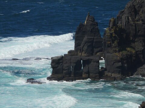 Rochers surplombant l'océan à Cliffs de Moher, Irlande, avec des vagues frappant les formations rocheuses.