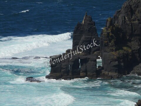 Rochers surplombant l'océan à Cliffs de Moher, Irlande, avec des vagues frappant les formations rocheuses.