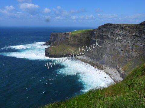 Falaises surplombant l'océan à Cliffs of Moher, Irlande, avec des vagues déferlant sur une plage de galets.