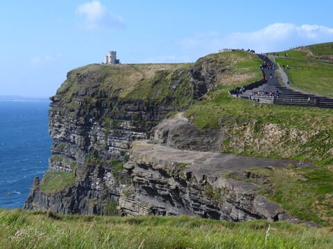 Falaises avec un château surplombant l'océan à Cliffs of Moher, Irlande. Des visiteurs se promenant sur un chemin en bord de falaise.