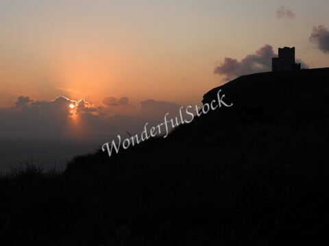 Coucher de soleil sur la falaise de Moher en Irlande, avec un bâtiment en silhouette sur la crête.