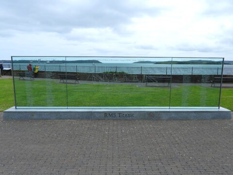 Mémorial en verre commémoratif du RMS Titanic à Cobh, Irlande, avec vue sur la mer et des bancs en arrière-plan.
