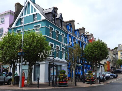 Maisons colorées à Cobh, Irlande, avec des arbres et des fleurs en pot sur le trottoir.