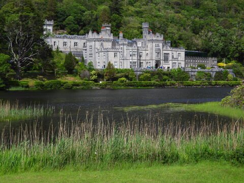 Château entouré de verdure, situé dans le Connemara, Irlande, avec un lac et des roseaux au premier plan.