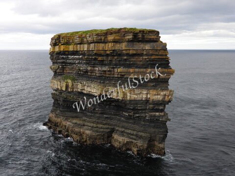 Un promontoire rocheux se dresse au bord de l'océan à Downpatrick Head, en Irlande, avec des strates de roches visibles et de l'herbe au sommet.