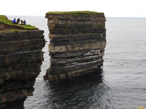 Falaises de Downpatrick Head en Irlande, avec des personnes assises sur l'herbe surplombant la mer.