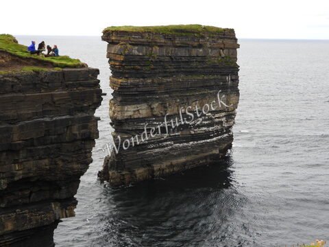 Falaises de Downpatrick Head en Irlande, avec des personnes assises sur l'herbe surplombant la mer.