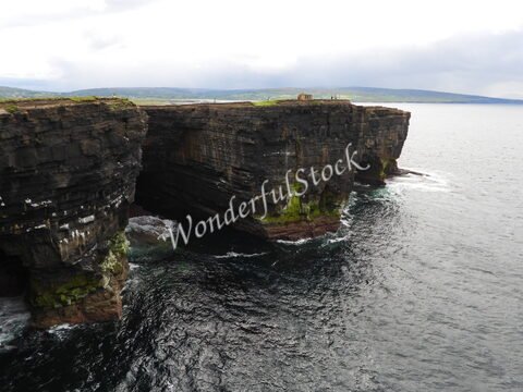 Falaises de Downpatrick Head en Irlande, avec des formations rocheuses maritimes et des vagues s'écrasant contre la côte.