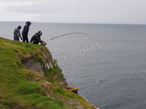 Pêcheurs au bord des falaises à Downpatrick Head, Irlande, avec la mer en arrière-plan et des herbes verdoyantes sur les rochers.