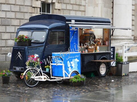 Un camion de nourriture décoré de fleurs à Dublin, Irlande, avec une petite remorque blanche et un panneau bleu.