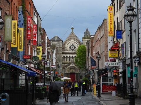 Rue animée avec des enseignes colorées et une église en arrière-plan à Dublin, Irlande.