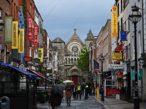 Rue animée avec des enseignes colorées et une église en arrière-plan à Dublin, Irlande.