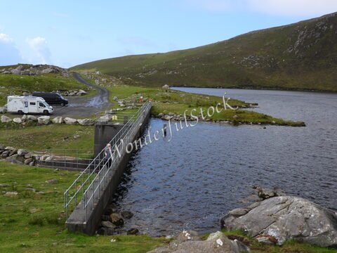 Rivière et route menant à un point d'accès en Irlande, avec des collines verdoyantes en arrière-plan.